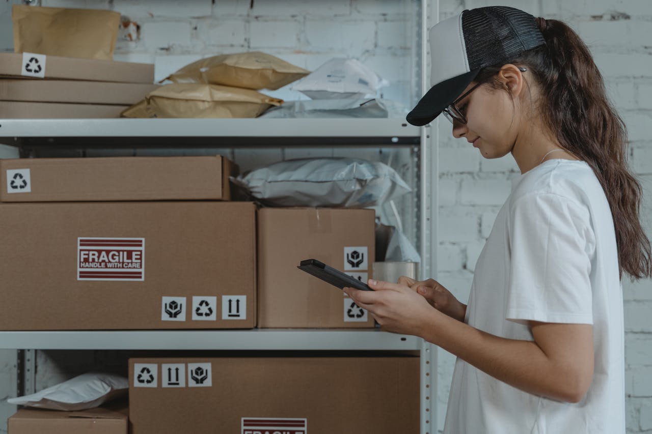 services-01 A female courier in uniform managing packages with a device in a storage room.